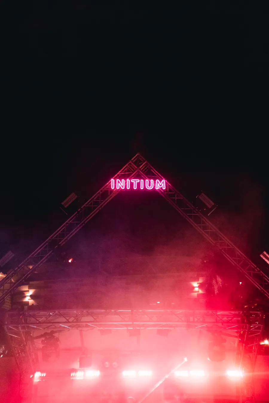 Letrero neón de Initium sobre el escenario entre el humo